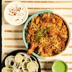 A flavorful bowl of Indian chicken biryani served with raita and onion salad, perfect for an aromatic meal.