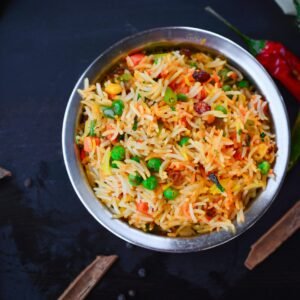 Top view of colorful biryani with vegetables in a metal bowl, showcasing Indian cuisine.